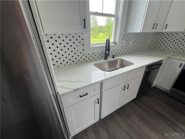 Kitchen featuring freestanding refrigerator, light stone counters, a sink, backsplash, and white cabinets | Image 9