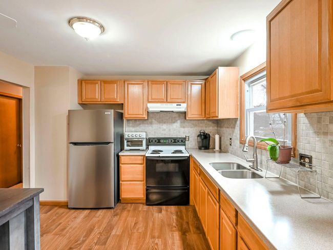 Kitchen featuring stainless steel refrigerator, sink, black range with electric cooktop, backsplash, and light wood-type flooring | Image 6