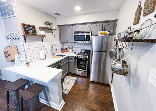 Kitchen featuring gray cabinets, open shelves, a sink, stainless steel appliances, and a peninsula | Image 6