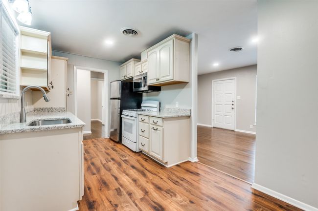 Kitchen with appliances, a sink, wood look finished floors, shelves, and light stone countertops | Image 9