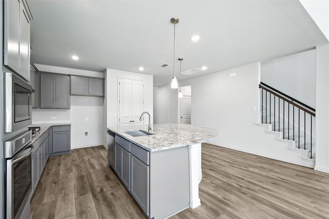Kitchen featuring appliances with stainless steel finishes, gray cabinets, wood finished floors, light stone countertops, and recessed lighting | Image 7
