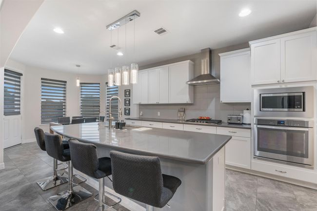 Sleek white cabinetry, a large island with seating, stainless steel appliances, and contemporary pendant lighting, creating a bright and inviting space. | Image 15