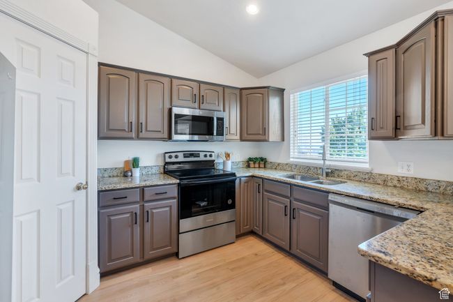 Kitchen featuring stainless steel appliances, a sink, lofted ceiling, light stone countertops, and light wood finished floors | Image 6