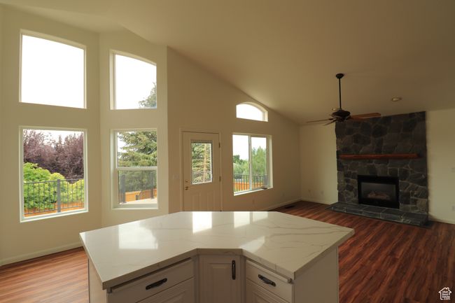 Kitchen featuring dark wood finished floors, white cabinetry, light stone counters, a fireplace, and high vaulted ceiling | Image 4