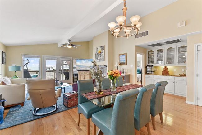 This spacious and bright living area features a modern open layout with hardwood floors, a cozy seating area, and a dining space with elegant lighting. Large windows and glass doors provide ample natural light and access to a balcony with views. The built-in cabinetry offers additional storage and display options. | Image 15