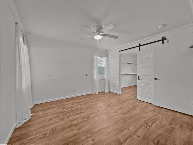Unfurnished bedroom with a barn door, light wood finished floors, and ceiling fan | Image 7