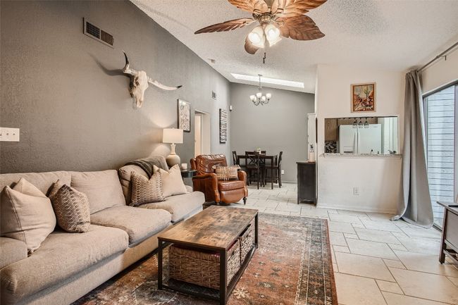 Living area with a textured ceiling, stone tile floors, vaulted ceiling, a ceiling fan, and a chandelier | Image 5