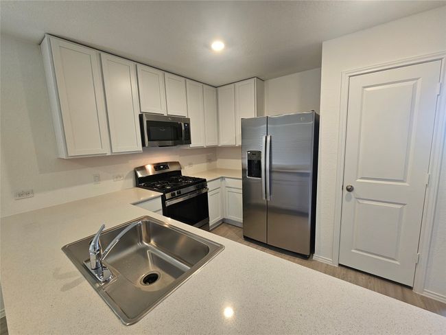 Kitchen featuring white cabinets, stainless steel appliances, light countertops, and a sink | Image 7