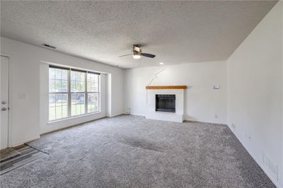 Unfurnished living room featuring carpet flooring, a brick fireplace, a textured ceiling, and ceiling fan | Image 3