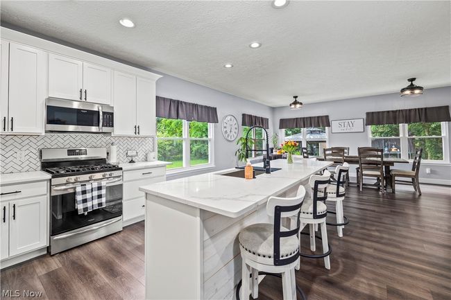 Kitchen with a center island with sink, dark wood-type flooring, sink, white cabinets, and appliances with stainless steel finishes | Image 16