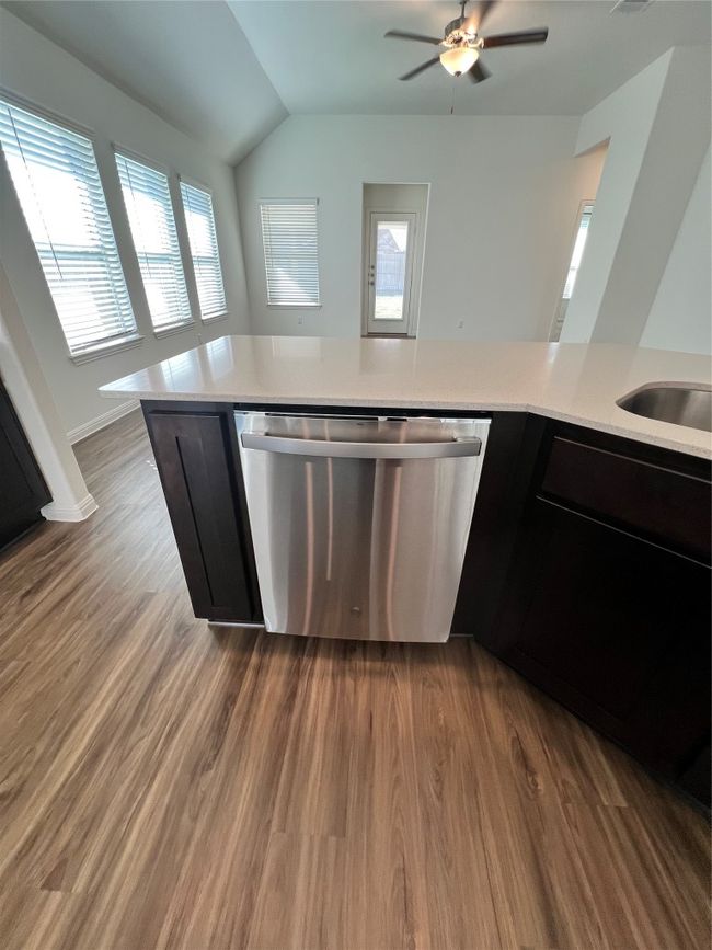 Kitchen featuring dark wood-style flooring, stainless steel dishwasher, dark cabinetry, plenty of natural light, and lofted ceiling | Image 12
