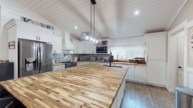 Kitchen featuring custom exhaust hood, dark hardwood / wood-style flooring, stainless steel appliances, butcher block counters, and a center island with sink | Image 11