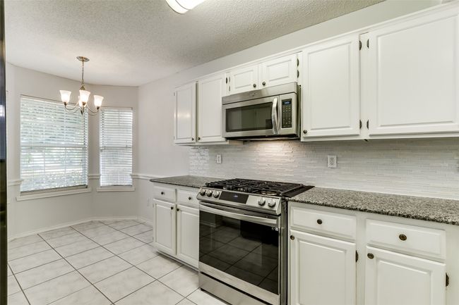Kitchen featuring backsplash, a notable chandelier, white cabinets, and appliances with stainless steel finishes | Image 13