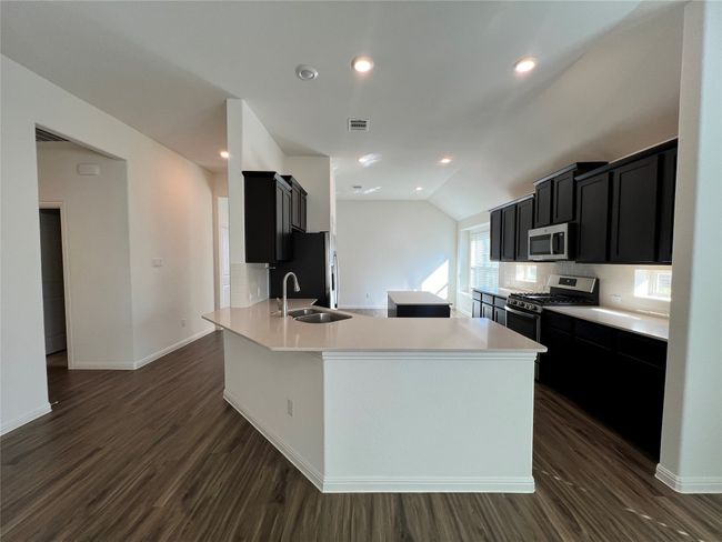 Kitchen with dark cabinetry, dark wood-style floors, a kitchen island, lofted ceiling, and decorative backsplash | Image 15