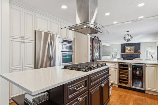 Gourmet kitchen with stainless steel appliances, double ovens, wine fridge, and a large center island featuring a gas cooktop and sleek quartz countertops. | Image 4