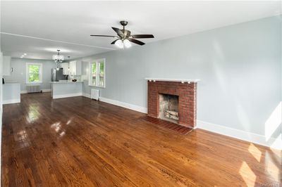 Unfurnished living room featuring ceiling fan with notable chandelier, radiator heating unit, wood-type flooring, and a fireplace | Image 3