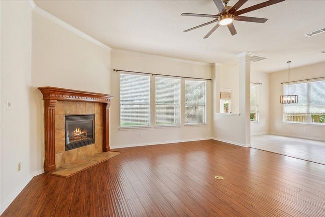 Unfurnished living room featuring a fireplace, a ceiling fan, wood finished floors, ornamental molding, and a chandelier | Image 11