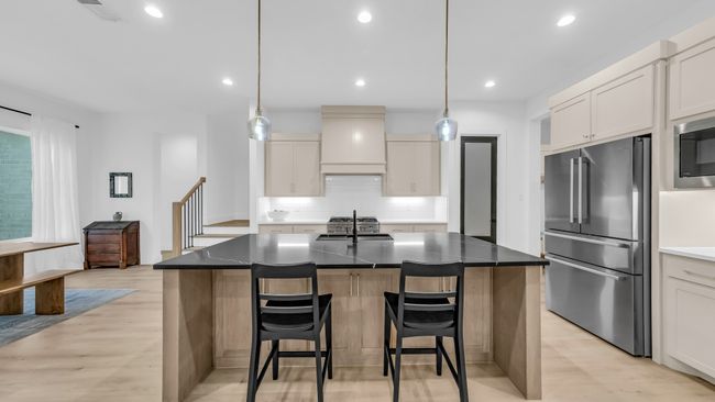 Kitchen featuring high end appliances, custom exhaust hood, backsplash, light wood-style flooring, and a kitchen breakfast bar | Image 18