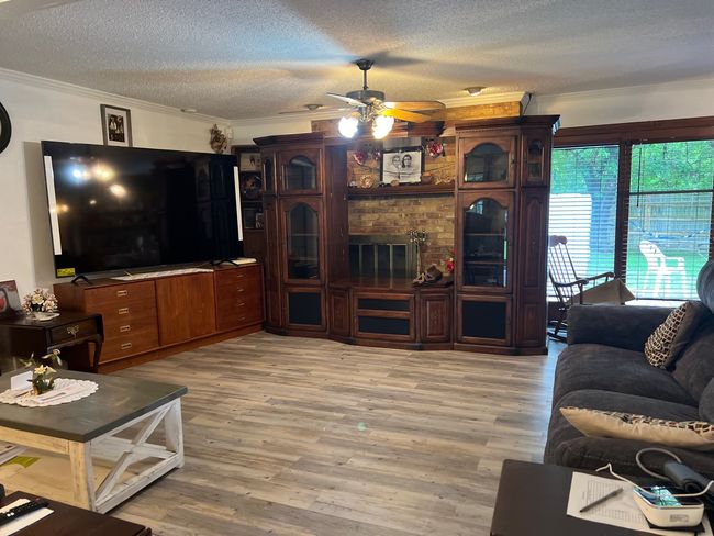 Den featuring light wood-type flooring, ceiling fan, a textured ceiling, and crown molding | Image 5