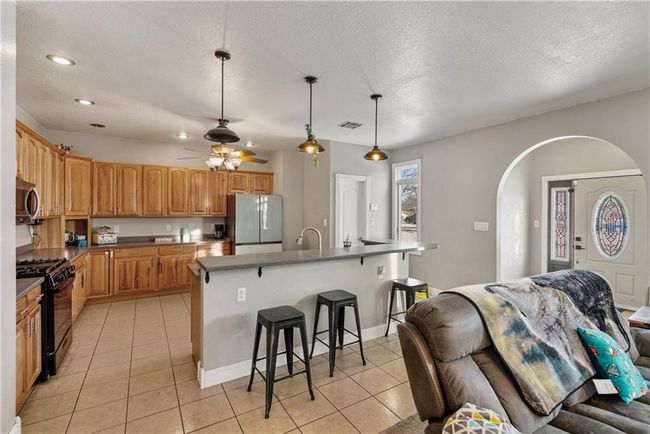 Kitchen featuring a breakfast bar area, black range with gas stovetop, white refrigerator, hanging light fixtures, and a center island with sink | Image 13