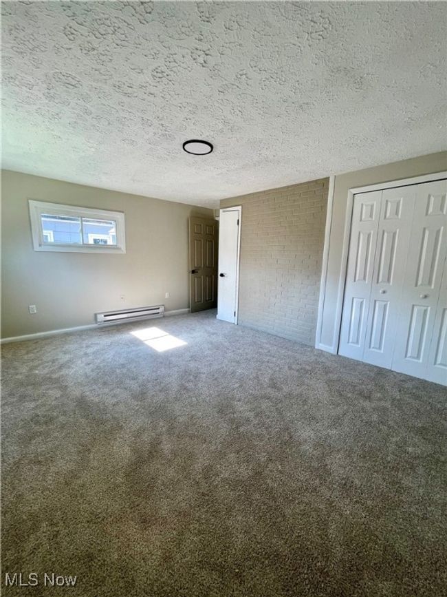 Unfurnished bedroom featuring carpet flooring, a baseboard radiator, multiple closets, and a textured ceiling | Image 17