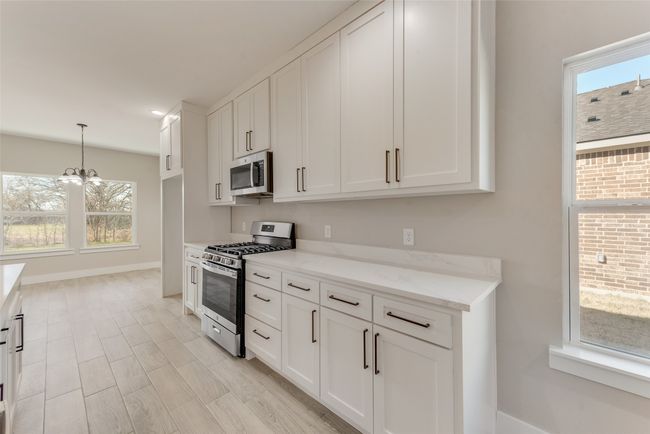 Kitchen with stainless steel appliances, a chandelier, white cabinetry, light stone countertops, and pendant lighting | Image 13