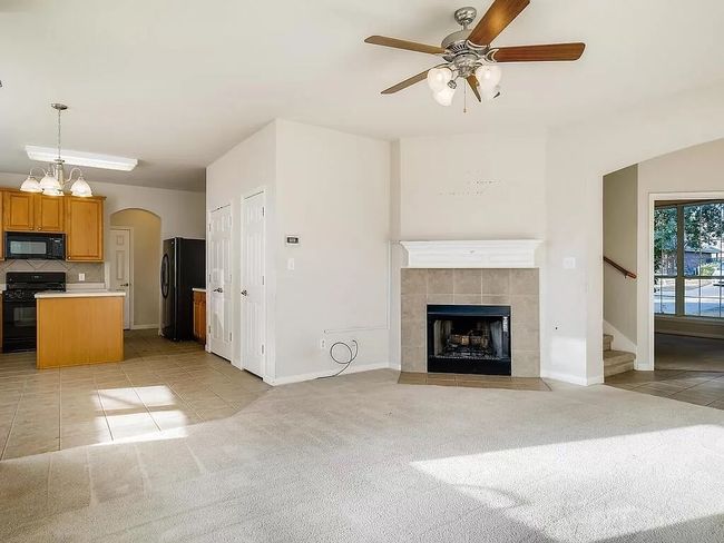 Unfurnished living room with a ceiling fan, light tile patterned floors, arched walkways, stairs, and a tiled fireplace | Image 7