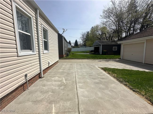 View of property exterior with a garage, a patio area, a yard, concrete driveway, and fence | Image 9