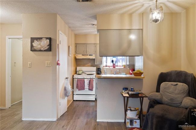 Kitchen with white electric stove, under cabinet range hood, wood finished floors, a textured ceiling, and baseboards | Image 5