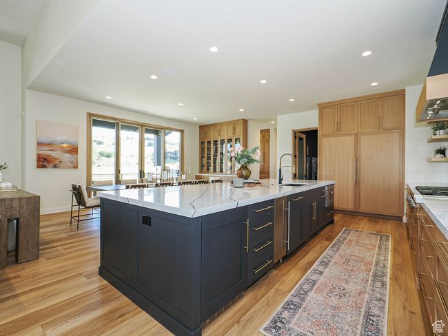Kitchen featuring recessed lighting, light wood-type flooring, ventilation hood, a large island with sink, and light stone countertops | Image 34