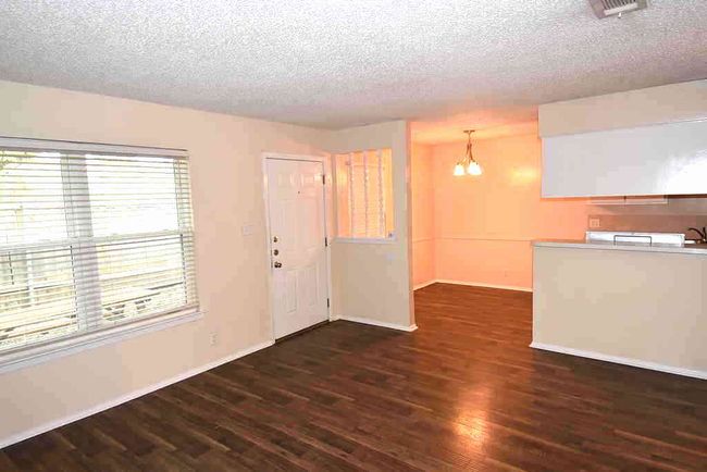 Unfurnished living room featuring a chandelier, dark wood finished floors, a textured ceiling, and baseboards | Image 6