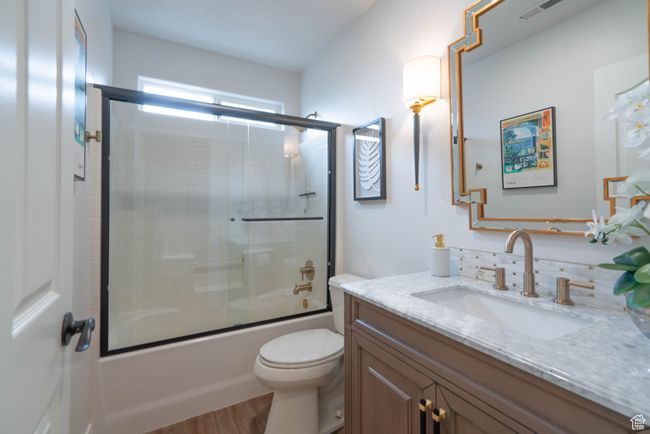 Full bathroom with toilet, bath / shower combo with glass door, hardwood / wood-style flooring, and vanity | Image 37