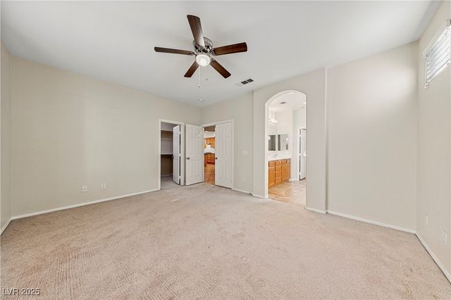 Unfurnished bedroom featuring light carpet, arched walkways, a spacious closet, connected bathroom, and ceiling fan | Image 28