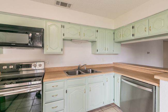 Kitchen with stainless steel appliances, a sink, light tile patterned floors, light countertops, and green cabinets | Image 10