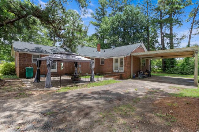 Back of house featuring brick siding, a gazebo, a chimney, an attached carport, and driveway | Image 4