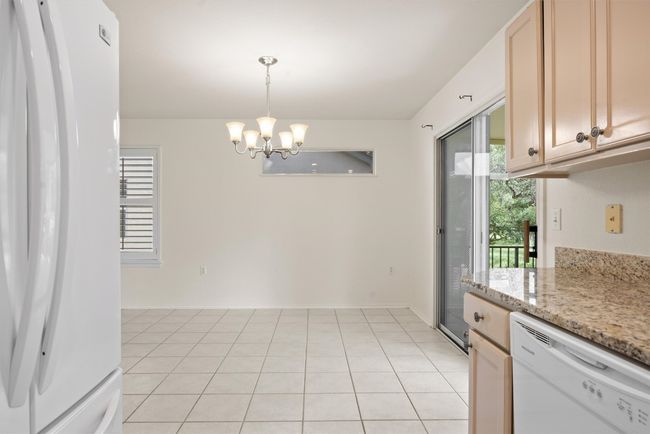 Kitchen featuring white appliances, a chandelier, decorative light fixtures, light tile patterned floors, and light stone counters | Image 21