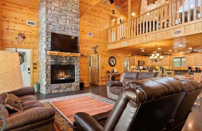 Living area featuring high vaulted ceiling, wooden walls, a stone fireplace, a chandelier, and wooden ceiling | Image 9