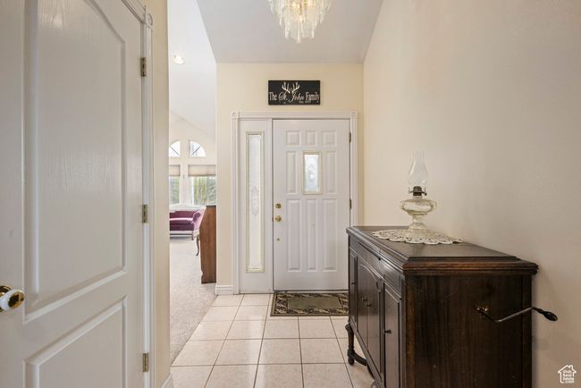 Entrance foyer with light colored carpet, baseboards, light tile patterned flooring, and a notable chandelier | Image 9