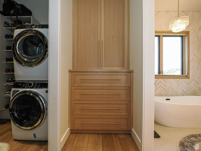 Washroom with stacked washer / dryer, a chandelier, and wood finished floors | Image 58