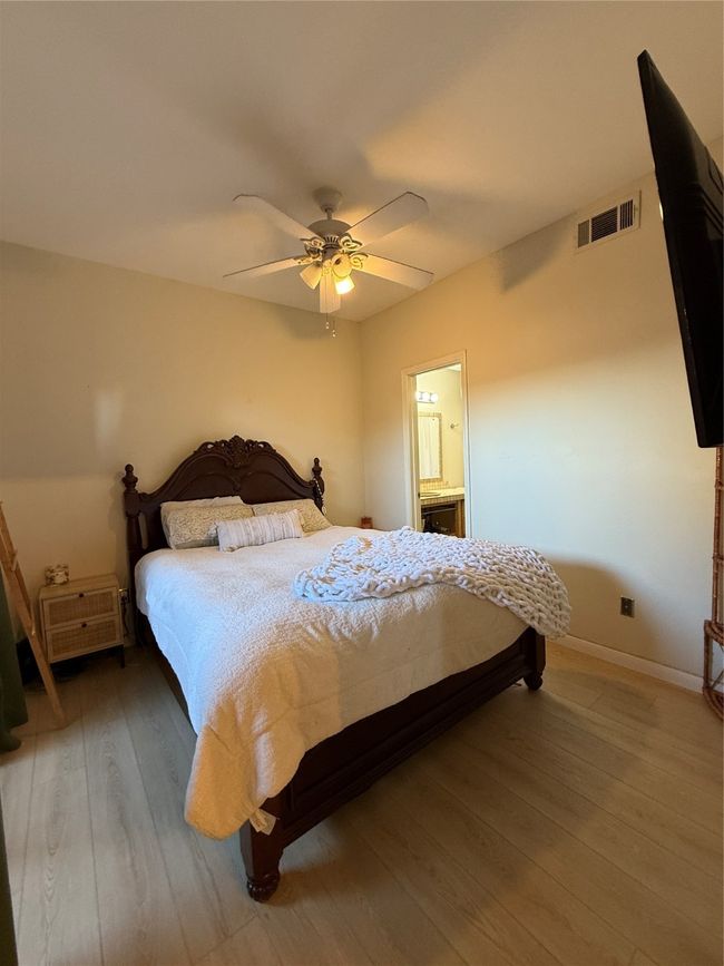 Bedroom with visible vents, connected bathroom, ceiling fan, wood finished floors, and baseboards | Image 28