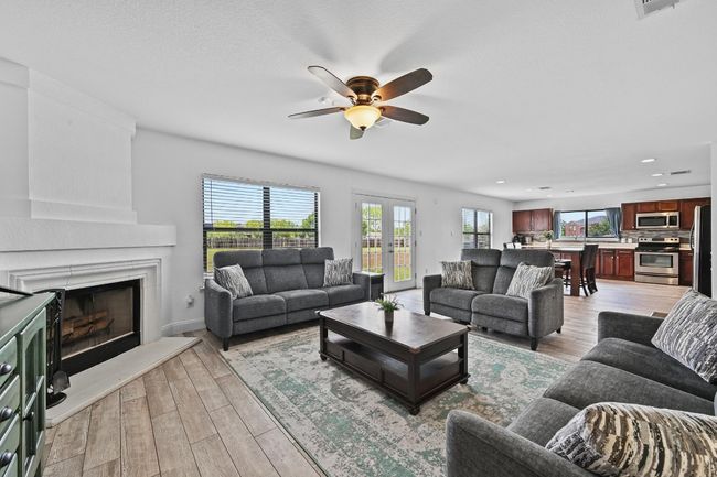 Living room with ceiling fan, a fireplace with raised hearth, light wood finished floors, and recessed lighting | Image 12