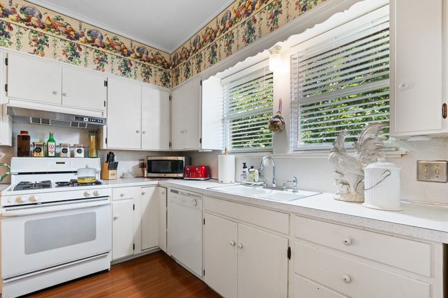 Kitchen featuring white appliances, a sink, under cabinet range hood, light countertops, and wallpapered walls | Image 14