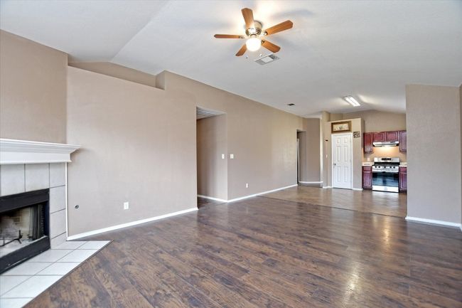 Unfurnished living room with lofted ceiling, a ceiling fan, dark wood-style flooring, a fireplace, and baseboards | Image 10