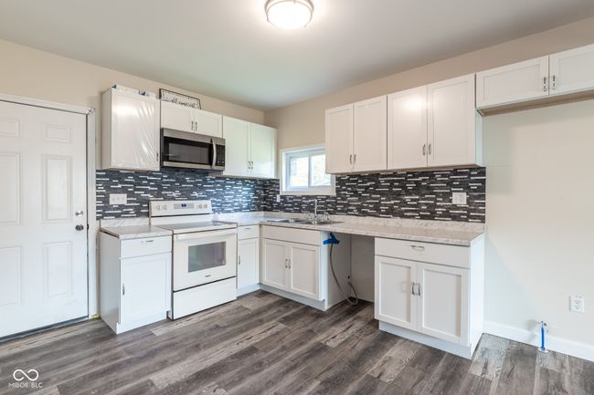 kitchen with stainless steel microwave, white cabinets, tasteful backsplash, a sink, and white electric stove | Image 14
