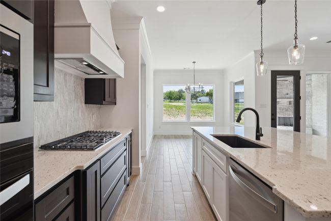 Kitchen featuring premium range hood, appliances with stainless steel finishes, sink, hanging light fixtures, and light stone countertops | Image 14