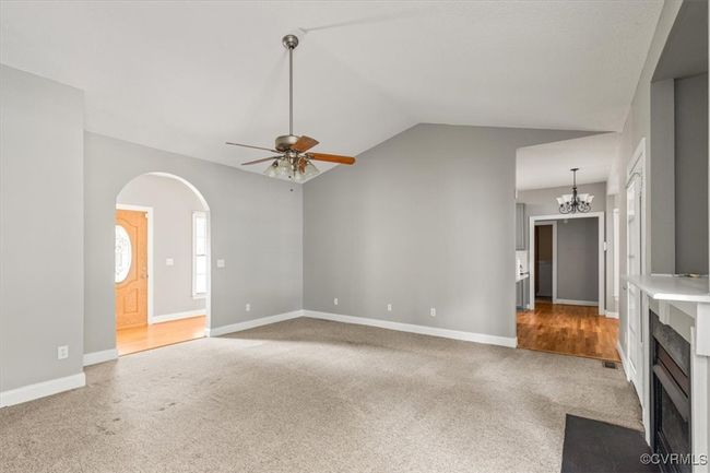 Unfurnished living room with a ceiling fan, carpet floors, a fireplace with flush hearth, baseboards, and lofted ceiling | Image 10