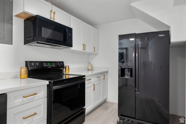 Kitchen with black appliances, white cabinetry, light wood-style floors, and light stone countertops | Image 8