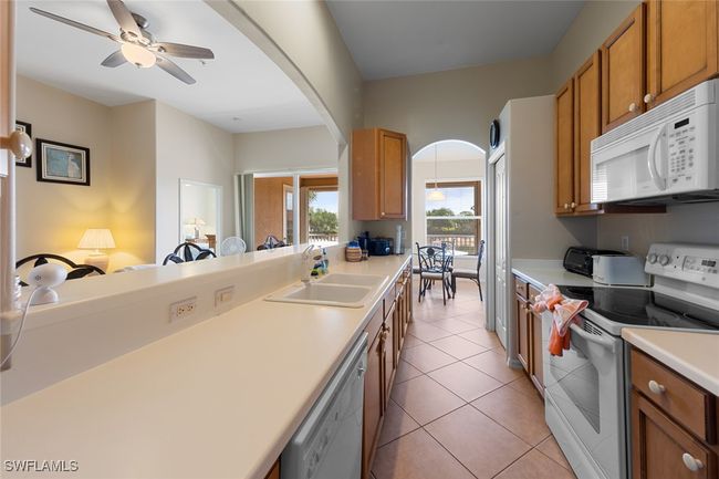 Kitchen with brown cabinets, light countertops, a sink, arched walkways, and white appliances | Image 11