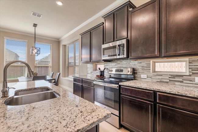 Kitchen with stainless steel appliances, a sink, crown molding, tasteful backsplash, and dark brown cabinetry | Image 11