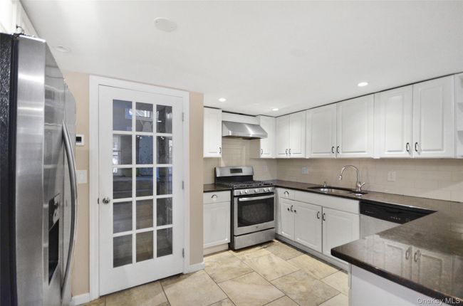 Kitchen with white cabinets, stainless steel appliances, decorative backsplash, wall chimney exhaust hood, and dark stone counters | Image 8